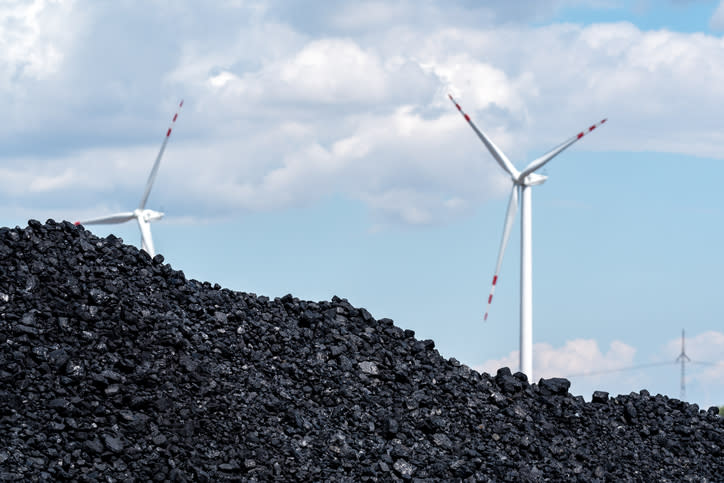 Wind turbines behind a pile of coal.