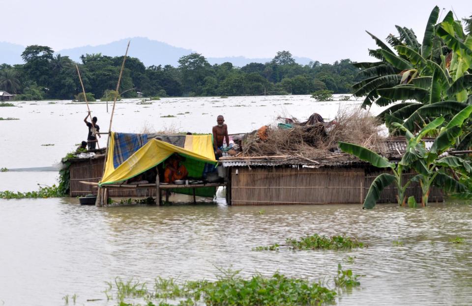 A family take shelter on the top of a hut in the flood-hit locality of Pavakity village in Morigaon district of Assam. (Photo credit should read Anuwar Ali Hazarika/Barcroft Media via Getty Images)