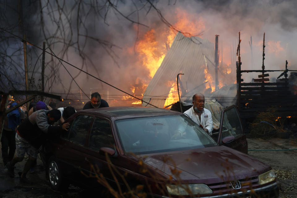 Residents push a car away from a burning forest fire engulfing homes in Villa Alemana, Valparaiso, Chile, Friday, Feb. 2, 2024. (Andres Pina, Aton Chile via AP)