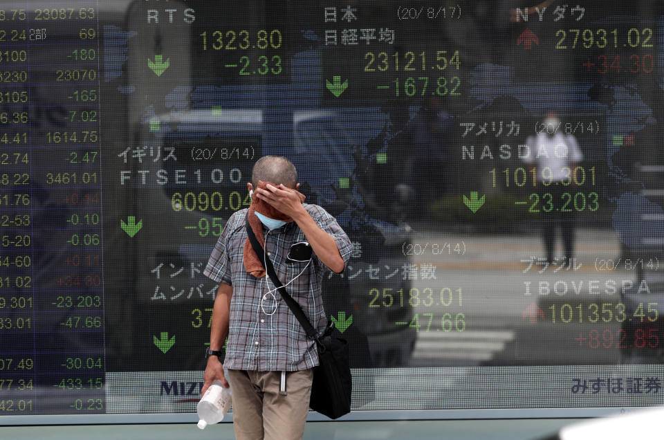 A man wipes his face in front of a monitor showing Japan's Nikkei 225 index and other stock exchanges from foreign countries in Tokyo on Monday, Aug. 17, 2020. Japanese stocks sank while other Asian markets gained Monday after Japan reported a record economic contraction as the coronavirus pandemic weighed on retailing, investment and exports.(AP Photo/Hiro Komae)