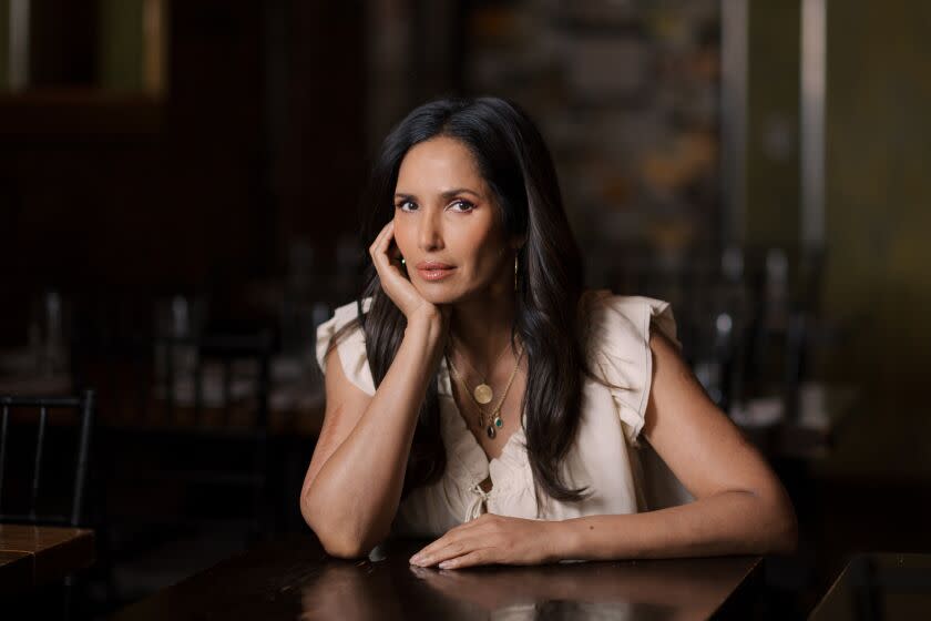 A woman sits at a table in a restaurant looking at the camera.