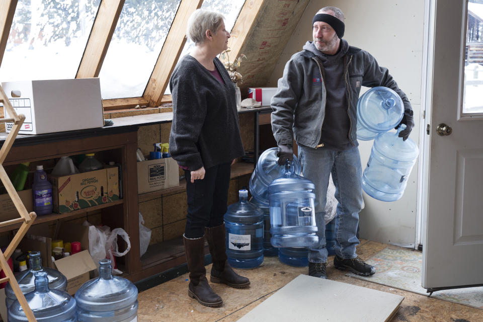 Catherine Maynard, a natural resource analyst for the U.S. Department of Agriculture, receives a bottled water delivery at her home in Rimini, Mont., by Bart Young of Big Spring Water on Feb. 18, 2019. About 30 households can’t drink their tap water because groundwater was polluted by about 150 abandoned gold, lead and copper mines that operated from the 1870s until 1953. (AP Photo/Janie Osborne)