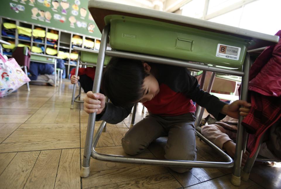 Students take shelter under desks during an earthquake simulation exercise at an elementary school in Tokyo March 11, 2014. (REUTERS/Yuya Shino)