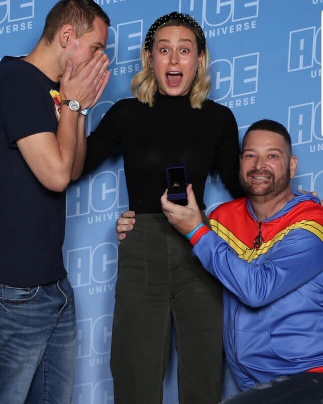 Brie Larson (center) was caught off-guard this weekend when fan&nbsp;John Chambrone (right) used his Comic-Con meet-and-greet with the "Captain Marvel" star to propose to his boyfriend,&nbsp;Richard Owen.&nbsp; (Photo: ACE Universe )