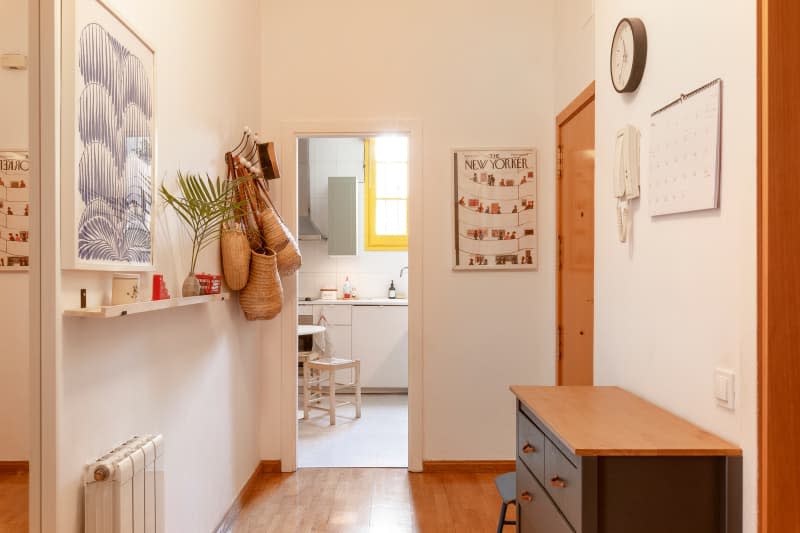 White entryway with hanging bags and baskets, floating shelf, and view into kitchen