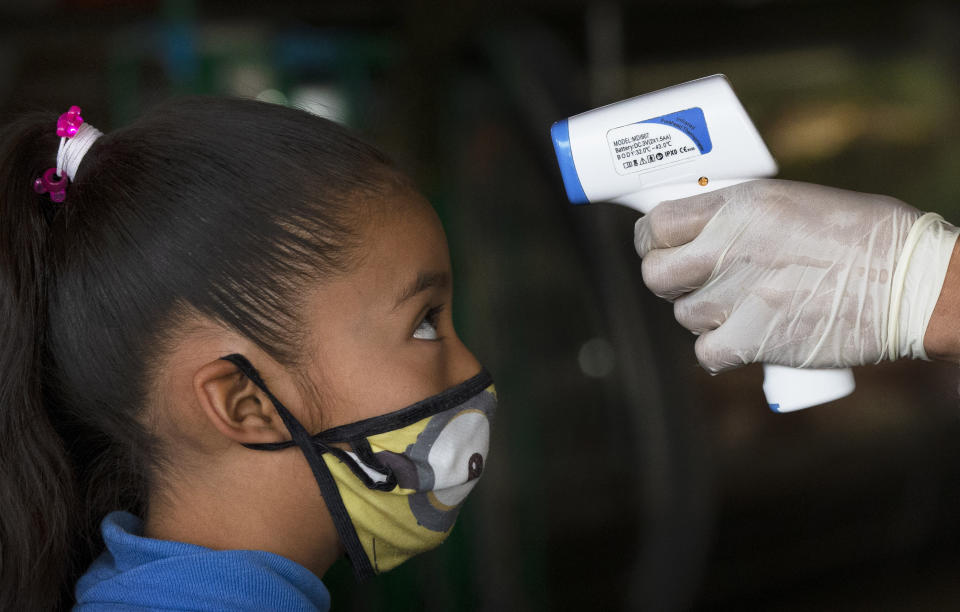 Un trabajador de la salud toma la temperatura de una niña para ayudar a aplanar la curva de contagios del nuevo coronavirus en el mercado Central de Abastos en Ciudad de México el jueves 18 de junio de 2020. (AP Foto/Marco Ugarte)