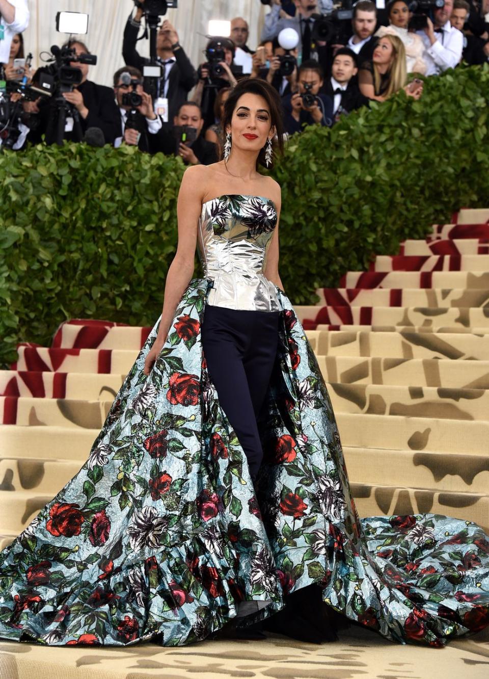 <p>Amal stuns on the red carpet of the Met Gala in a metallic top, navy pants, and a long train covered in roses by British designer Richard Quinn.</p>