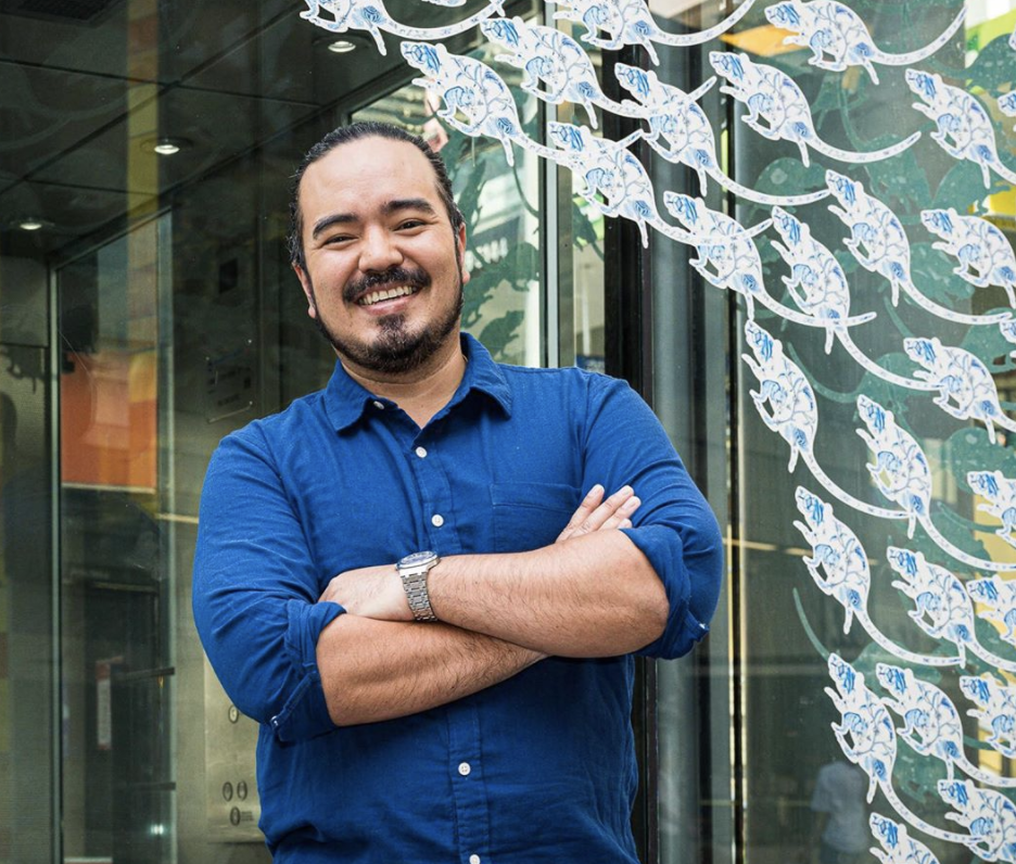 MasterChef season two winner Adam Liaw wears a blue shirt and poses in front of a glass door