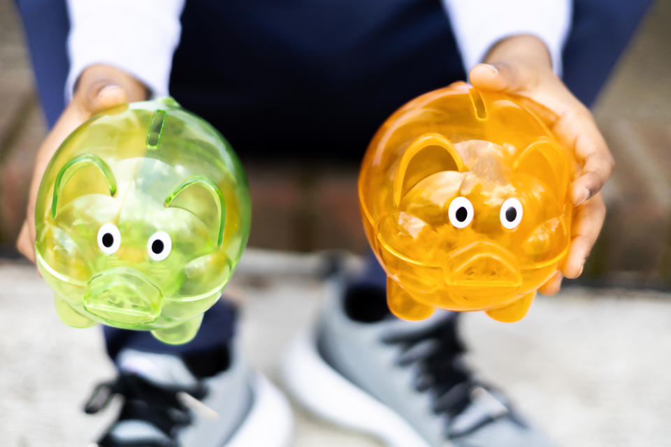 conceptual image of need to save for cost of raising children with young black boy holding 2 colorful empty piggy banks ~ shot with canon eos rp