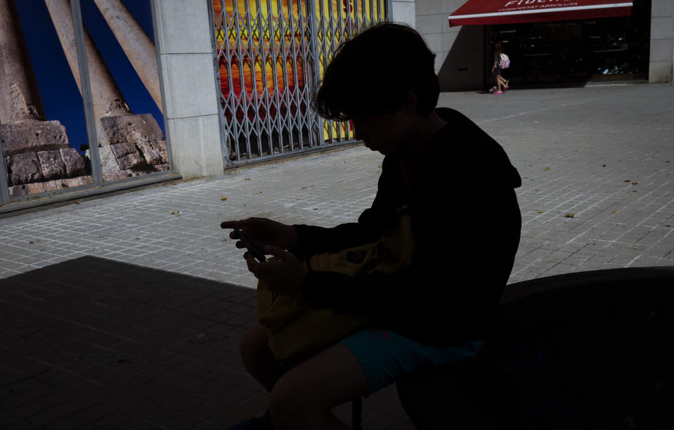 A 12-year-old boy plays with his personal phone outside school in Barcelona, Spain, Monday, June 17, 2024. Parents across Europe are rallying to make it normal for young kids to live smartphone-free. From Spain to Ireland and the UK, groups are ballooning on chat groups like WhatsApp and agreeing to link arms and refuse to buy children younger than 12 smartphones. (AP Photo/Emilio Morenatti)