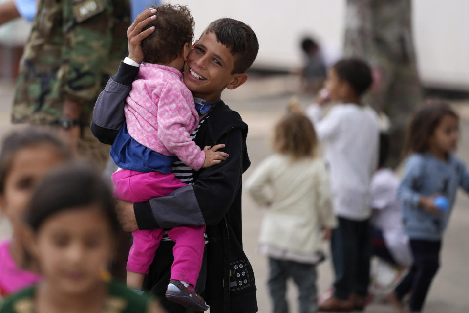 A recently evacuated young Afghan boy carries a child at the Ramstein U.S. Air Base, Germany, Tuesday, Aug. 24, 2021. The largest American military community overseas housed thousands of Afghan evacuees in an increasingly crowded tent city. (AP Photo/Matthias Schrader)