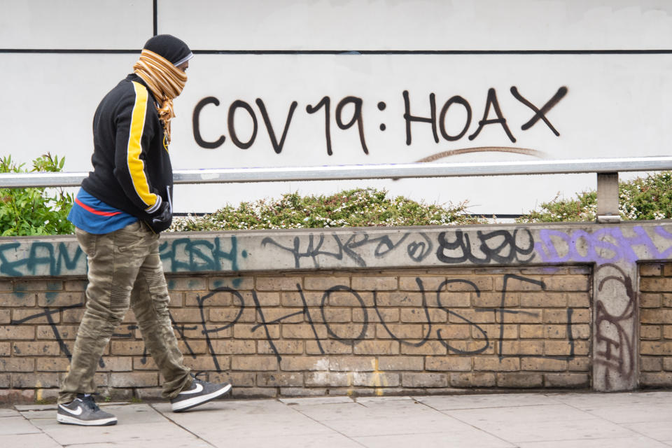 A man passes graffiti reading 'cov 19: hoax', in south London, as the UK continues in lockdown to help curb the spread of coronavirus.