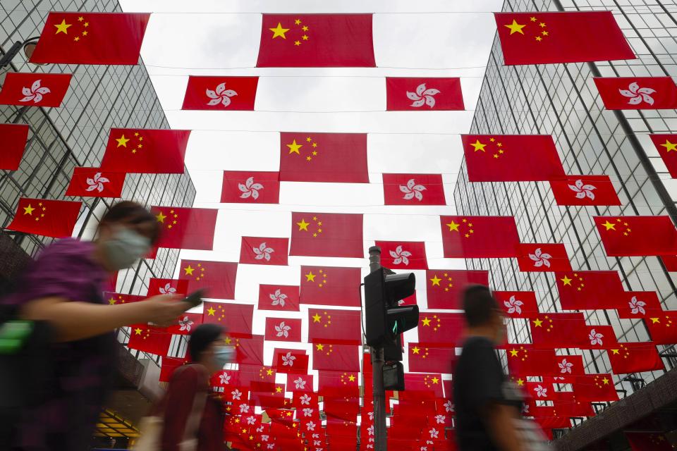 FILE - In this Sunday, June 27, 2021, file photo, people walk past China national flags and Hong Kong flags for the celebration of 24th anniversary of Hong Kong handover to China at a shopping district in Hong Kong. A year after Beijing imposed a harsh national security law on Hong Kong, the civil liberties that raised hopes for more democracy are fading. (AP Photo/Vincent Yu, File)