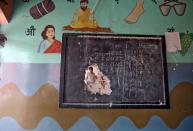 A man is seen through a hole on a classroom wall after the school building was attacked by a mob in a riot affected area following clashes between people demonstrating for and against a new citizenship law in New Delhi