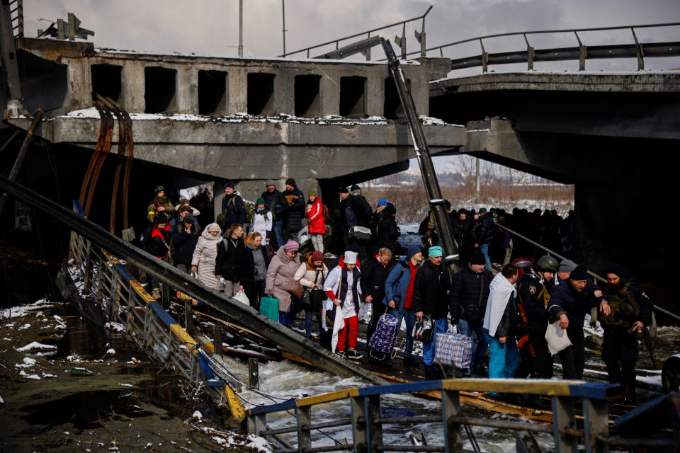 People file across a makeshift river crossing below a destroyed bridge as they flee from advancing Russian troops whose attack on Ukraine continues in the town of Irpin outside Kyiv, Ukraine, March 8, 2022. REUTERS/Thomas Peter