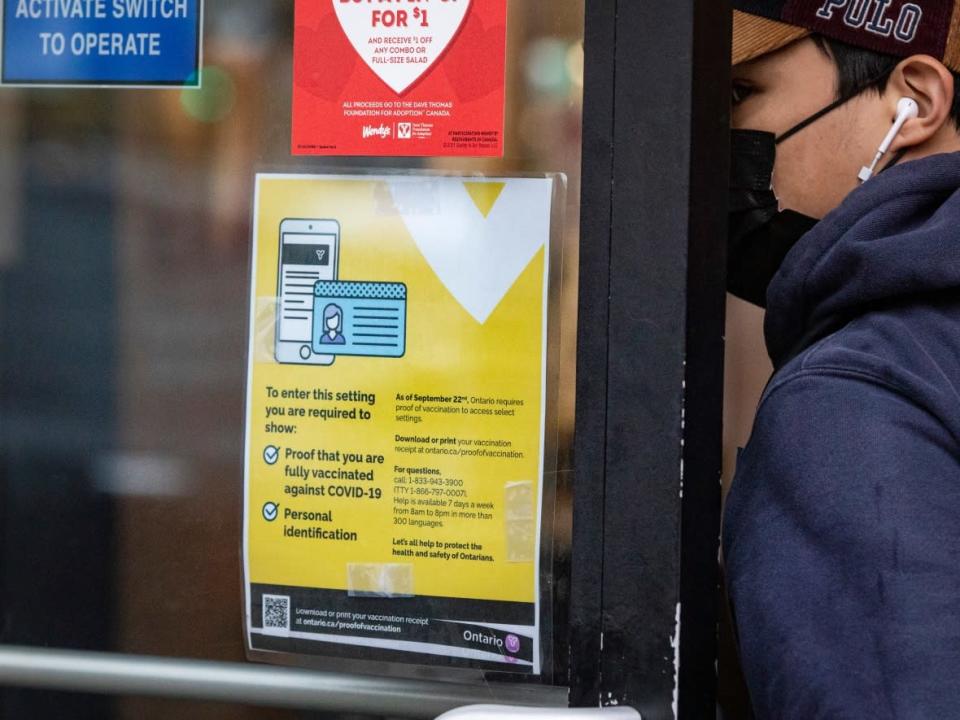 A patron enters a fast-food restaurant past a sign displaying proof of vaccination information. (Evan Mitsui/CBC - image credit)