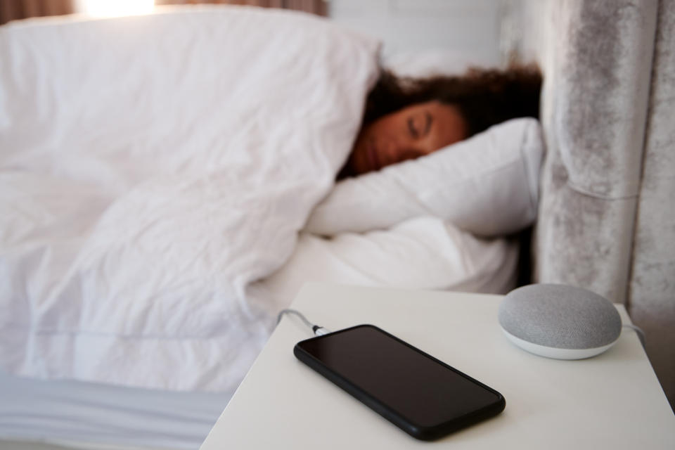Woman Asleep In Bed With Mobile Phone And Voice Assistant On Bedside Table