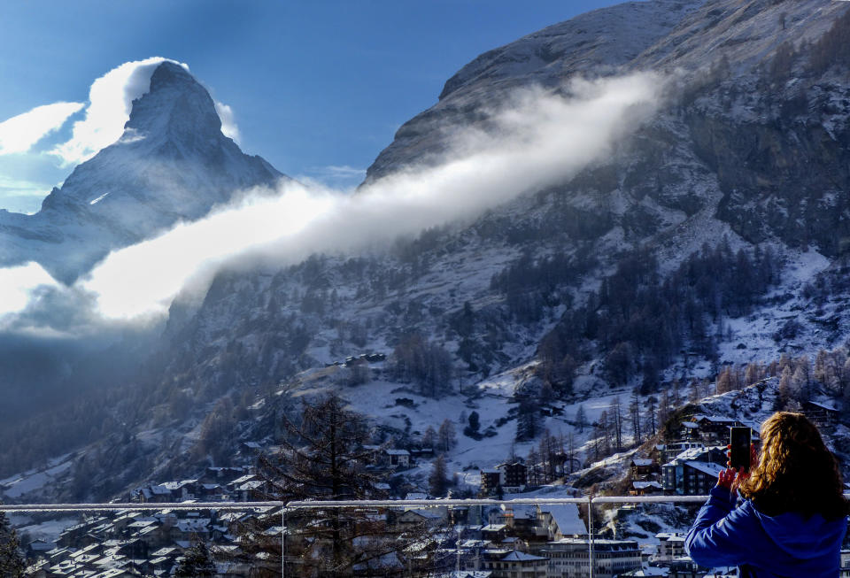 A woman takes a picture the Matterhorn, left, in Zermatt, Switzerland, Wednesday, Dec.2, 2020. Zermatt is home to one of the Swiss ski stations that has become an epicenter of discord among Alpine neighbors. EU member states Austria, France, Germany and Italy are shutting or severely restricting access to the slopes this holiday season amid COVID-19 concerns, Switzerland is not. (AP Photo/Jamey Keaten)