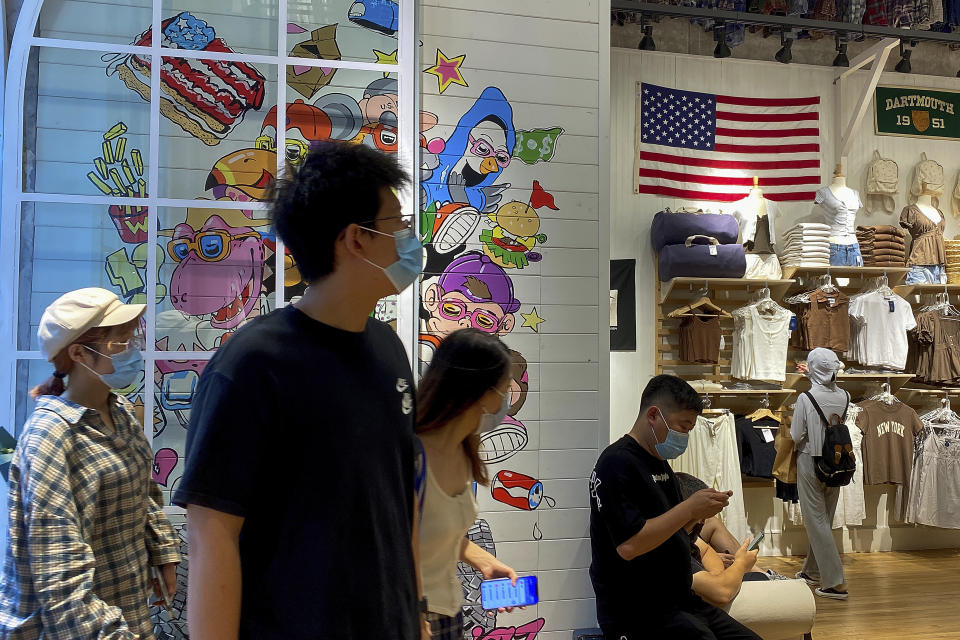 People wearing face masks visit a fashion boutique displaying an American flag in Beijing, Sunday, July 11, 2021. China on Sunday said it will take "necessary measures" to respond to the U.S. blacklisting of Chinese companies over their alleged role in abuses of Uyghur people and other Muslim ethnic minorities. (AP Photo/Andy Wong)