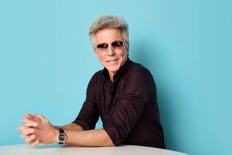 man in sunglasses sitting against a blue background
