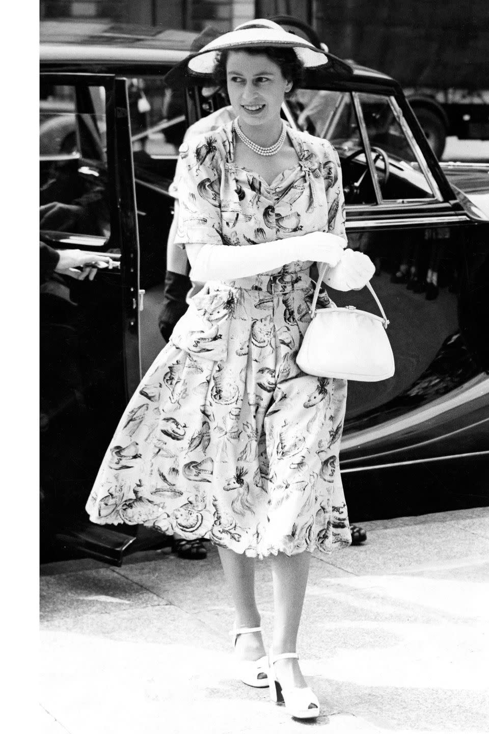 <p>Here she is in a printed knee-length dress, sun hat, white gloves, handle bag, and peep toe heels. </p>