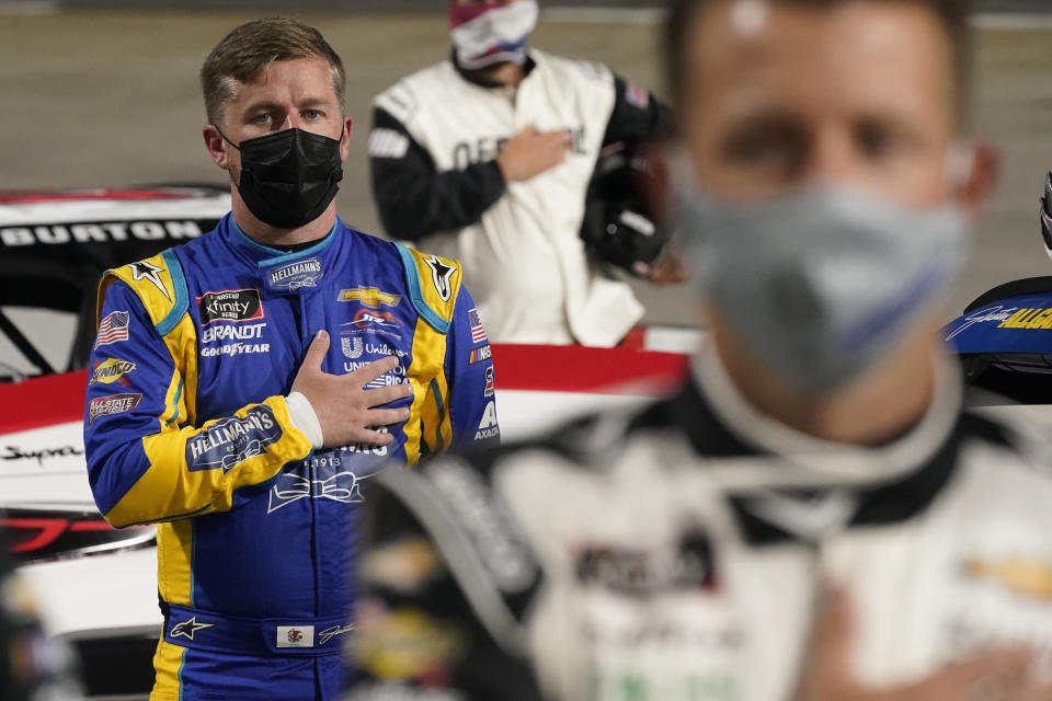 Justin Allgaier, left, and AJ Allmendinger, front, stand during the national anthem before the NASCAR Xfinity Series auto race at Martinsville Speedway in Martinsville, Va., Friday, April 9, 2021. (AP Photo/Steve Helber)