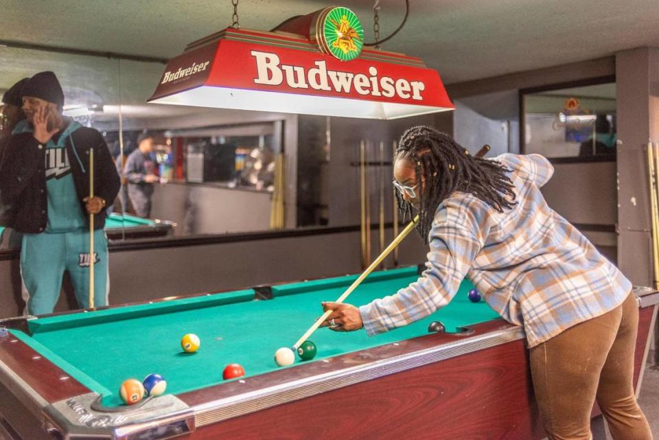 Rosalyn Brown aims for the corner pocket while her billiards competitor Timothy Williams chats with a friend just out of the frame.
