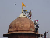 Sikhs hoist a Nishan Sahib, a Sikh religious flag, on a minaret of the historic Red Fort monument in New Delhi, India, Tuesday, Jan. 26, 2021. Tens of thousands of protesting farmers drove long lines of tractors into India's capital on Tuesday, breaking through police barricades, defying tear gas and storming the historic Red Fort as the nation celebrated Republic Day. (AP Photo/Dinesh Joshi)