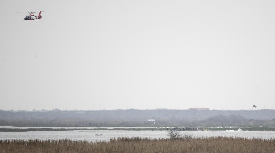 A helicopter flies overhead as emergency personnel work the scene of a plane crash site in Trinity Bay in Anahuac, Texas on Saturday, Feb. 23, 2019. The Federal Aviation Administration said a Boeing 767 cargo plane went down approximately 30 miles southeast of Houston's George Bush Intercontinental Airport. (Brett Coomer/Houston Chronicle via AP)