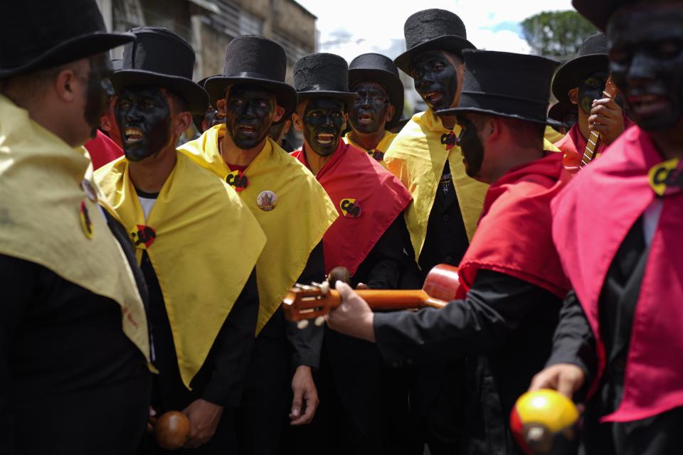 Devotos, vestidos con ropas coloniales y pañuelos que representan los colores de partidos políticos de esa época y con las caras pintadas de negro, participan en la popular fiesta de la Parranda de San Pedro en Guatire, Venezuela, el jueves 29 de junio de 2023. (AP Foto/Ariana Cubillos)