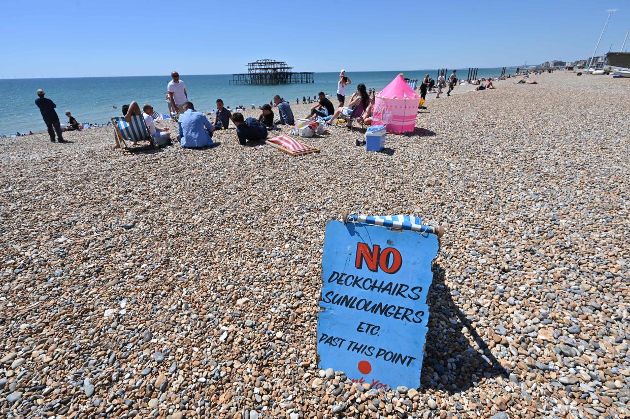 TOPSHOT - People sunbathe on the beach in front of the derelict West Pier in Brighton, on the south coast of England on May 31, 2020 on the eve of a further relaxation of the novel coronavirus lockdown rules. - The UK government has set out a gradual easing of lockdown measures in England, with socially distanced groups of six friends and families allowed to meet in parks and gardens from June 1. (Photo by Glyn KIRK / AFP) (Photo by GLYN KIRK/AFP via Getty Images)