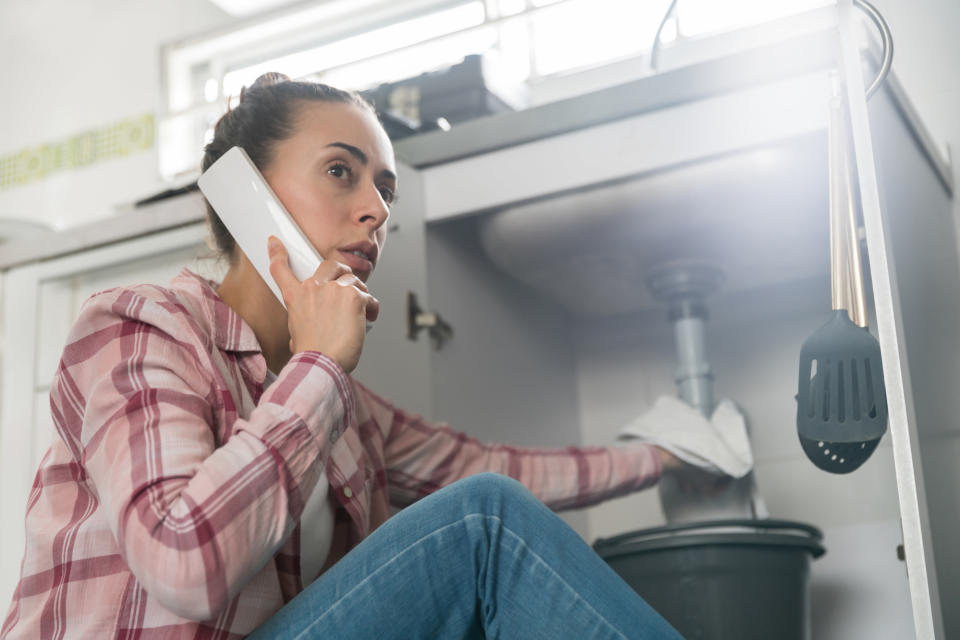 Woman holding a towel underneath a sink while talking on the phone to someone