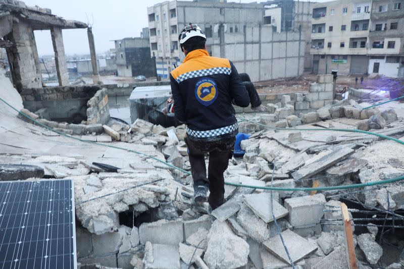 A rescue worker carries a child at the site of a damaged building, following an earthquake, in rebel-held Azaz