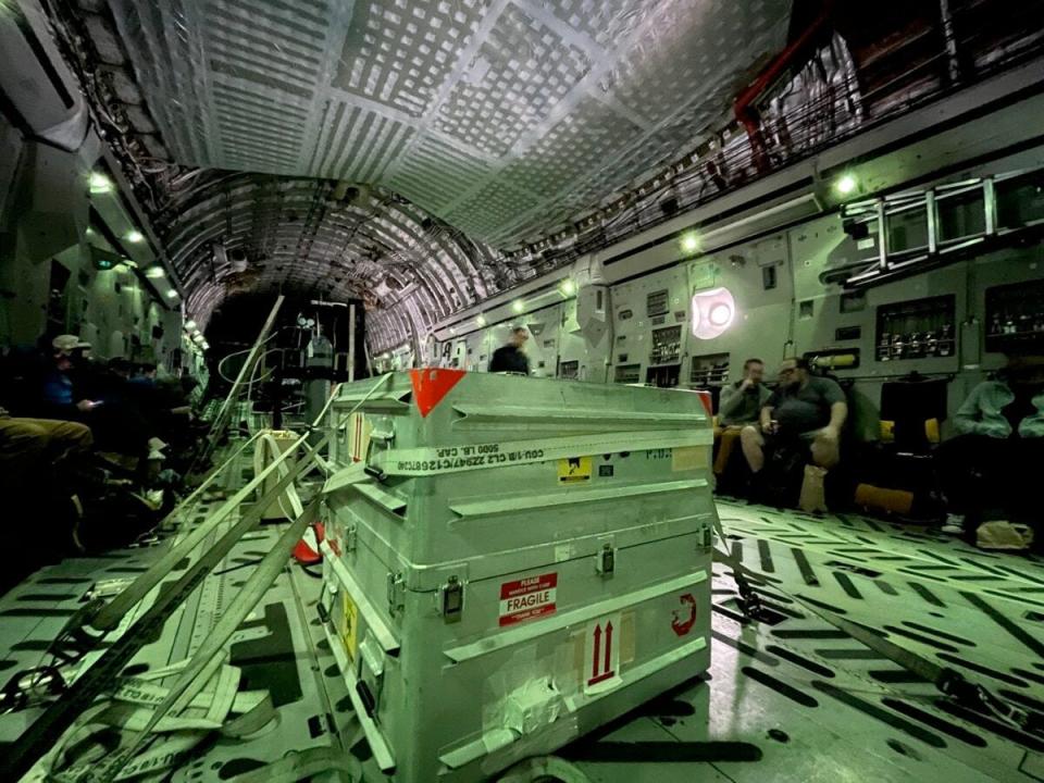 A metal shipping container marked fragile onboard a U.S. Air Force C-17 aircraft with several people in the background