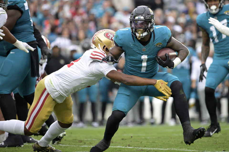 Jacksonville Jaguars running back Travis Etienne Jr. (1) runs as San Francisco 49ers cornerback Deommodore Lenoir, left, defends during the first half of an NFL football game, Sunday, Nov. 12, 2023, in Jacksonville, Fla. (AP Photo/Phelan M. Ebenhack)