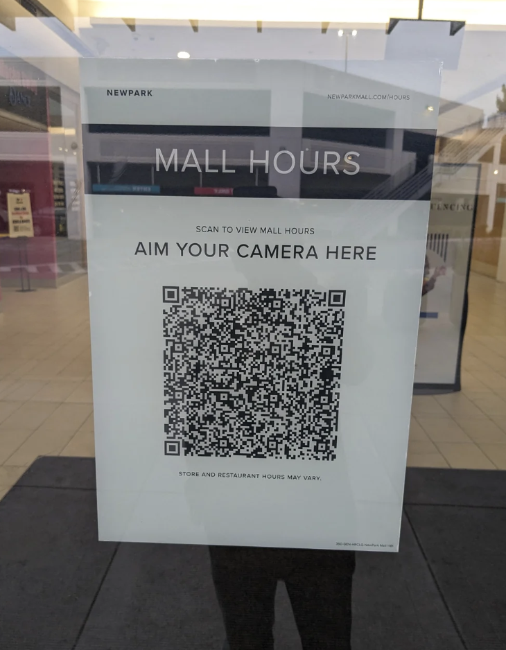 Sign with a QR code for viewing mall hours, text above reads "SCAN TO VIEW MALL HOURS"