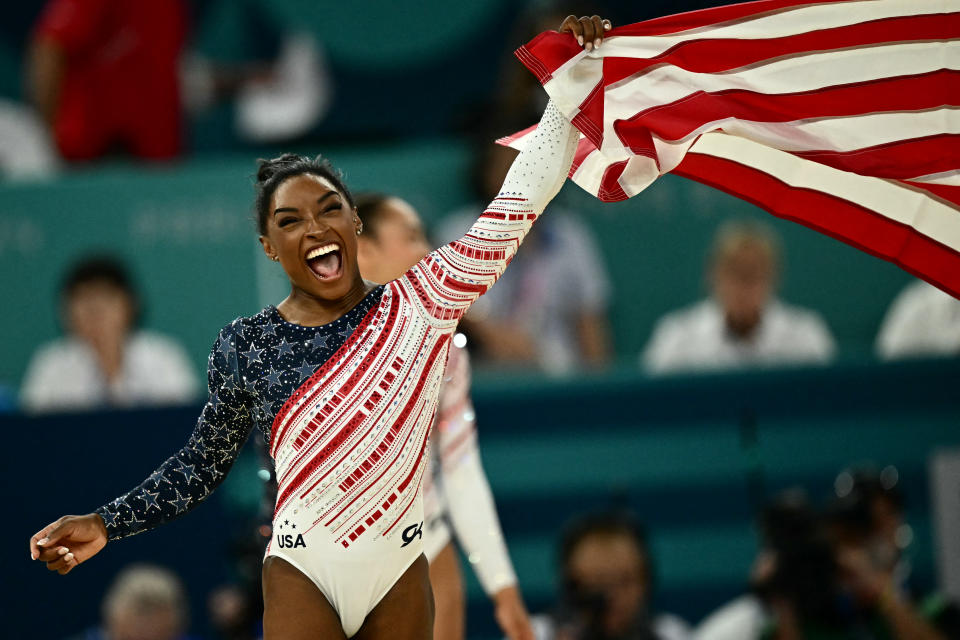 Biles waves an American flag after Team USA's victory at the Paris 2024 Olympic Games.