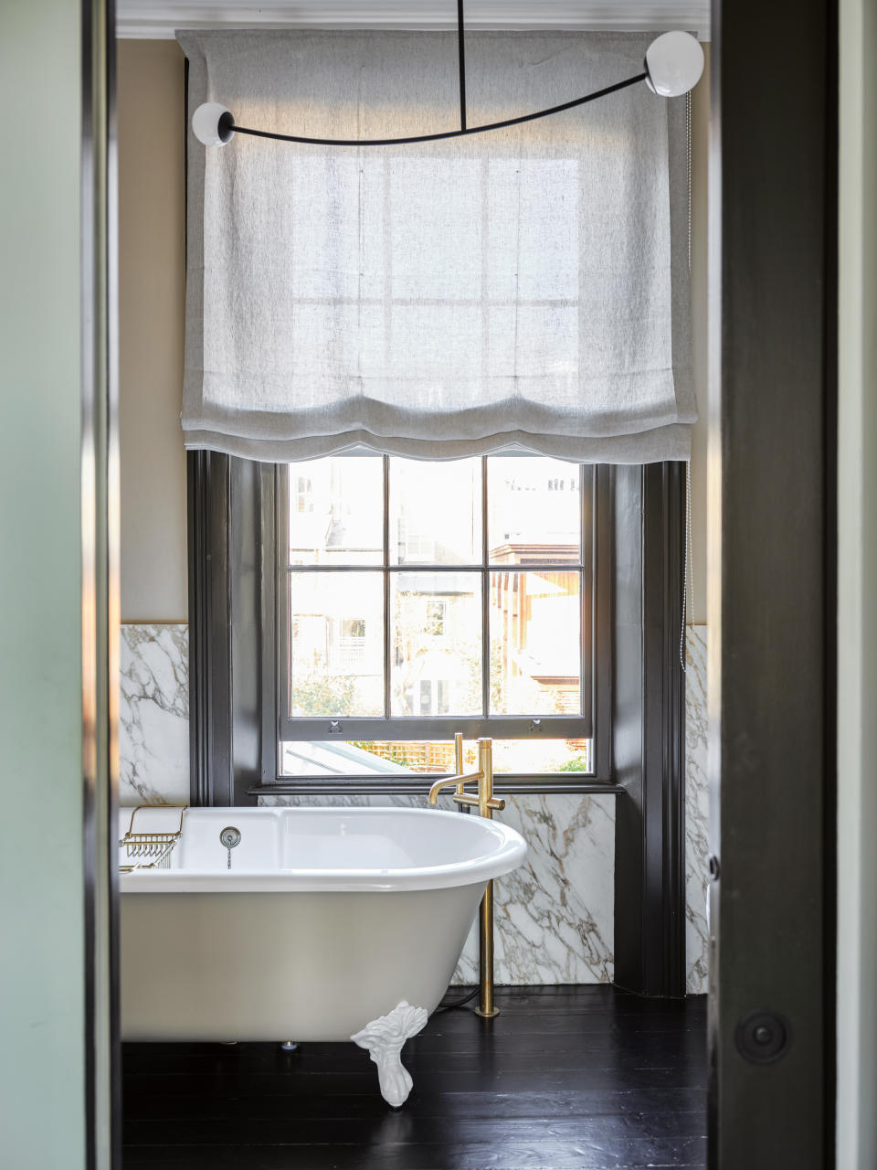 freestanding bath in dark and marble bathroom with large window