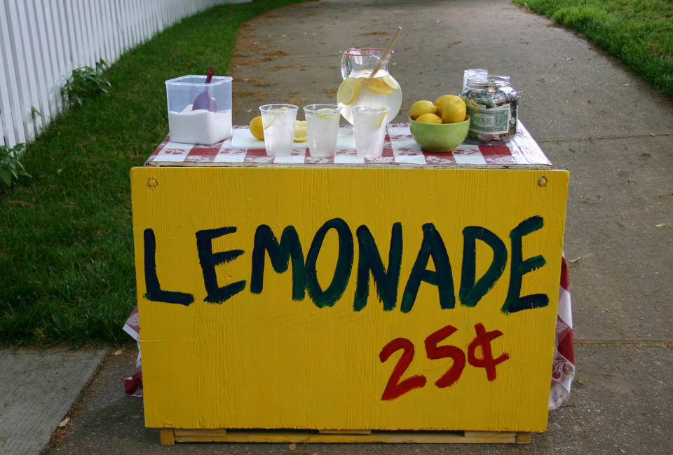 Pictured is a classic lemonade stand on a footpath advertising the beverage for 25 cents. 