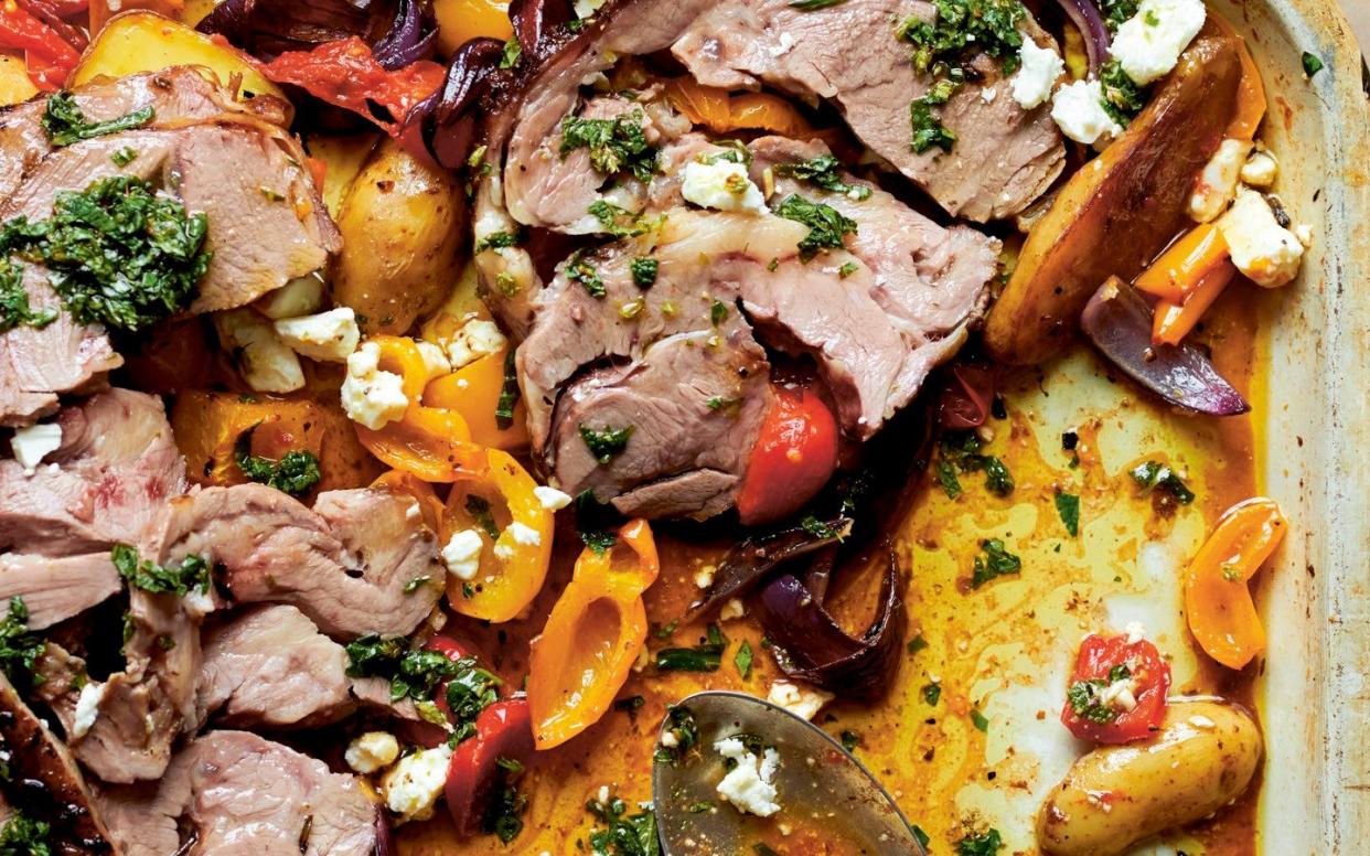 A roasting dish filled with lamb, red and yellow peppers, feta and herbs in a juicy tomato sauce