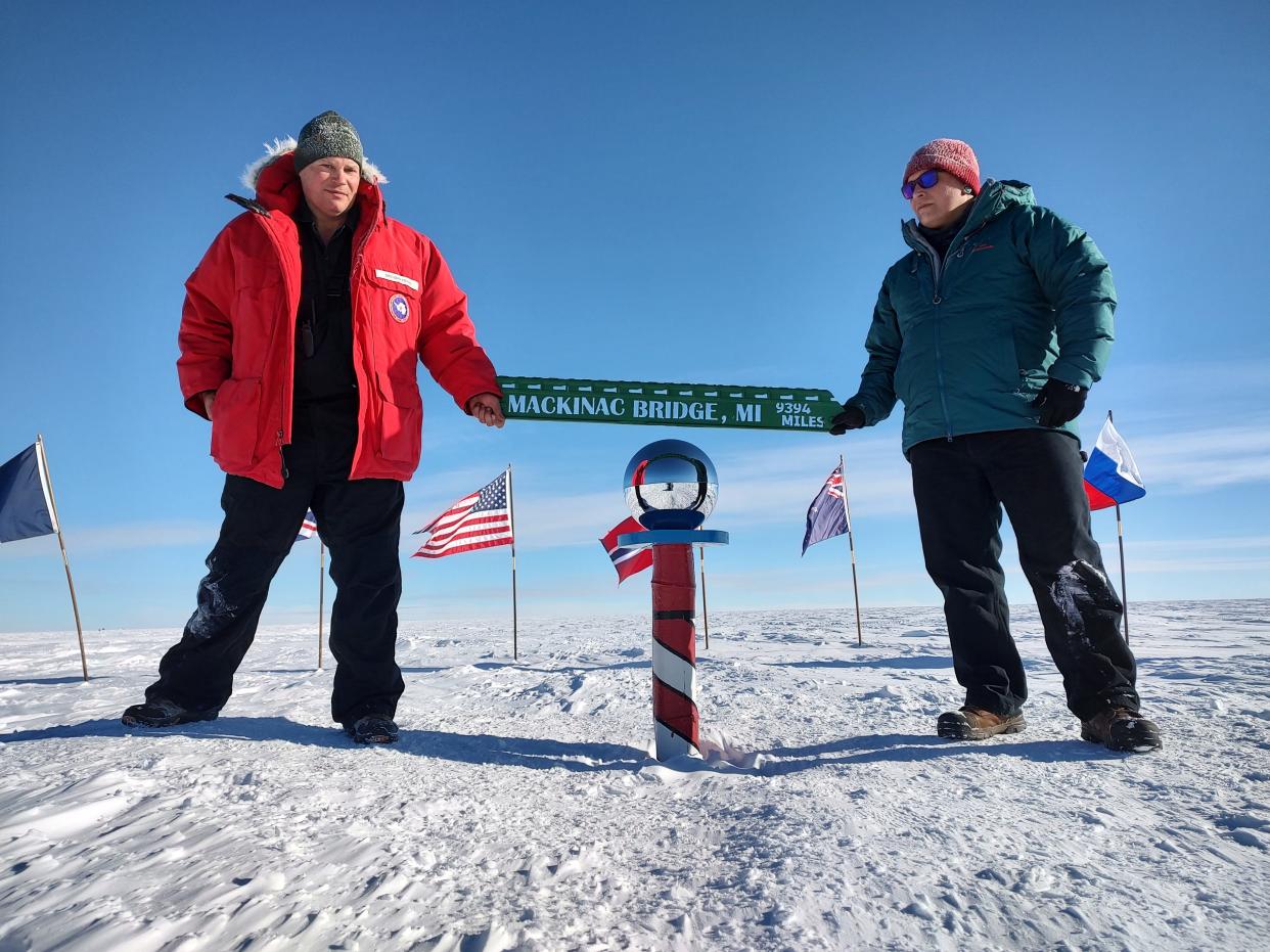 Brendan Fisher (left) and Troy Leighton pose at the South Pole with a sign Fisher made with steel from the Mackinac Bridge deck grating, listing the distance to the Mackinac Bridge from Antarctica.