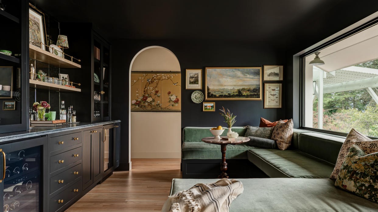  Living room with dark blue painted walls and ceiling, sage green velvet banquette seating and built-in bar. 