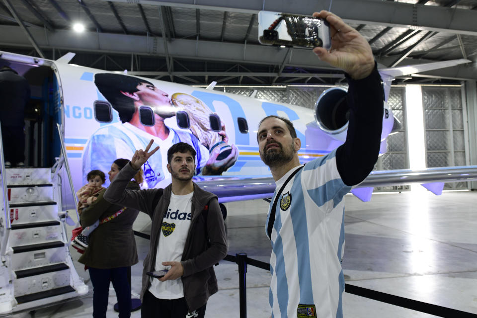 Aficionados posan para selfies durante la presentación de una aeronave dedicada al fallecido futbolista, en una base militar en Morón, en las afueras de Buenos Aires, Argentina, el sábado 23 de julio de 2022. El avión partirá después en una gira por el mundo, que visitará Brasil, Colombia, México y Estados Unidos antes de llegar a Europa y hacer parada en Roma y Nápoles _dos lugares míticos en la carrera del 10_ y aterrizar en el Mundial de Catar. (AP Foto/Gustavo Garello)