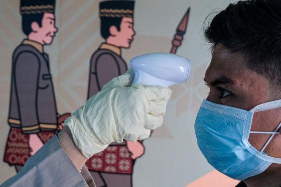 A person checks the temperature of a passenger wearing a facemask as he arrives at the Sultan Mahmud Badaruddin II International airport in Palembang (AFP via Getty Images)