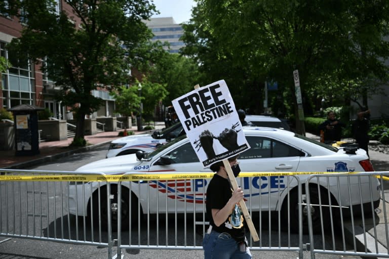 A demonstrator holds a sign as a police vehicle and barricades block a road after officers cleared a pro-Palestinian student protest encampment at George Washington University on May 8, 2024 (Brendan SMIALOWSKI)