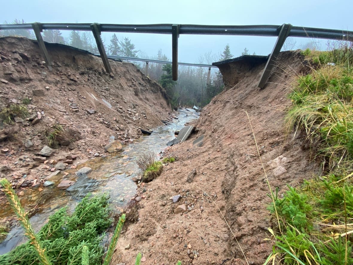 Asphalt lies in a rushing body of water at the base of Little Smokey near Ingonish, N.S., after a storm last week washed out a bridge.  (Craig Paisley/CBC - image credit)