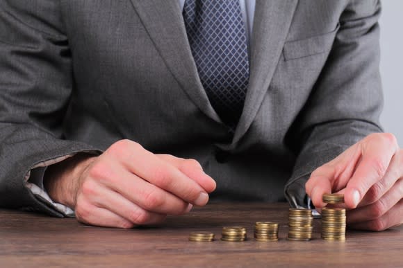 Businessman stacking coins on a table, in piles of increasing height.