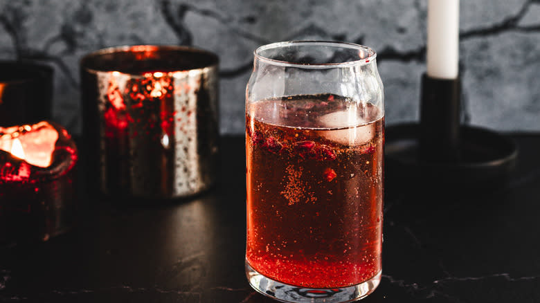 Red cocktail glass in front of candles and pomegranate