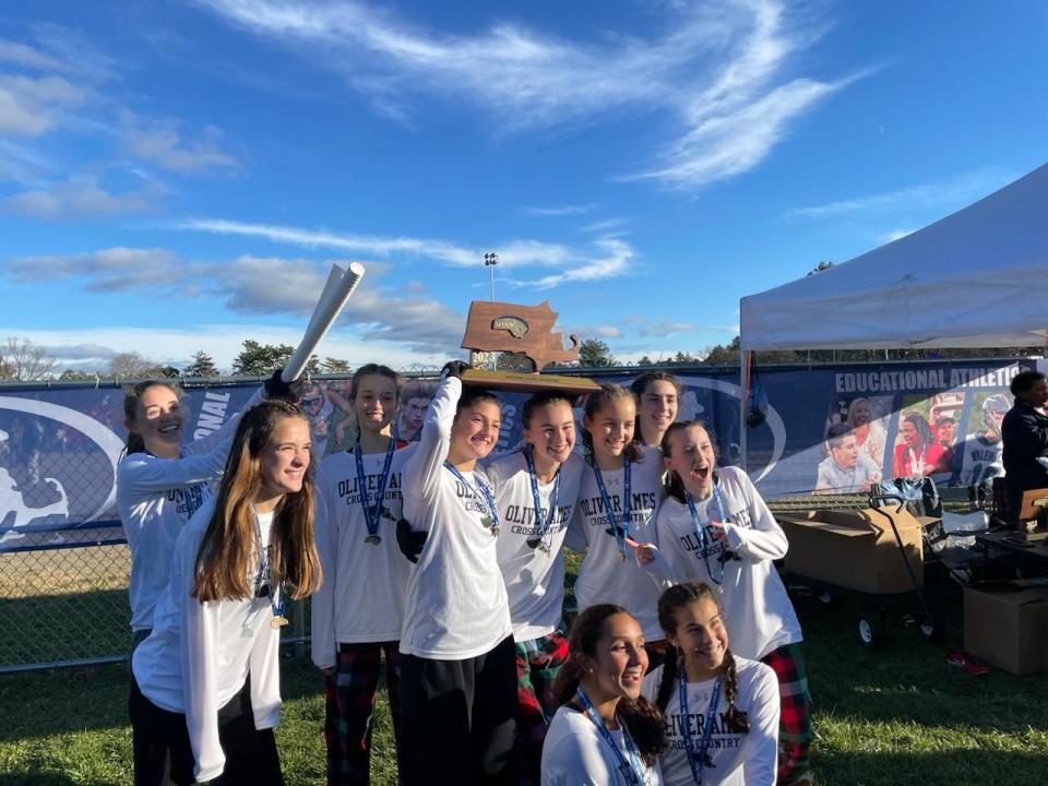 Members of the Oliver Ames High girls cross country team celebrate after winning the Division 1 team crown at Fort Devens on Saturday, Nov. 18, 2023.