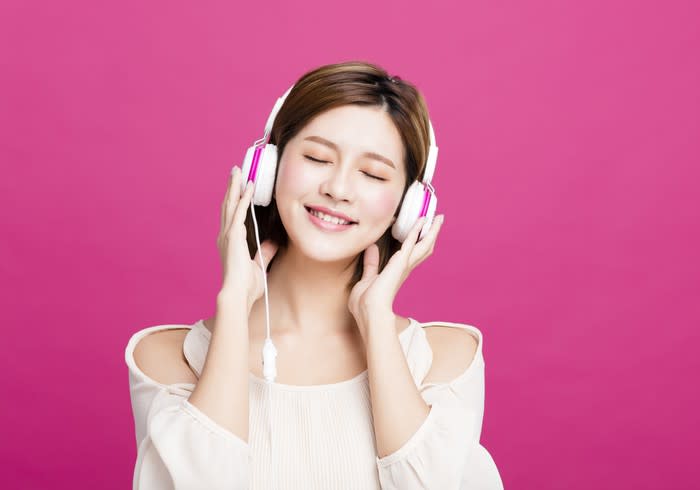 A young woman listening to music on white-and-pink headphones.